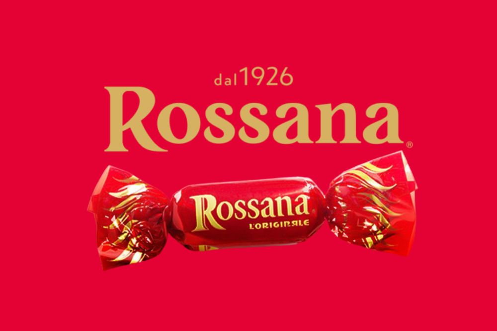 Caramella Rossana l’Originale avvolta nell’iconico incarto rosso e dorato, con il nome del marchio e la scritta "dal 1926" sopra su uno sfondo rosso uniforme.