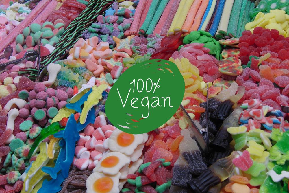 Assortimento colorato di caramelle gommose veganedisposte in file su una bancarella, tra cui sour strips, gummy eggs, cola bottle e altre forme di frutta.
