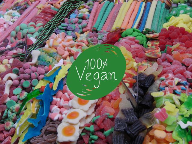 Assortimento colorato di caramelle gommose veganedisposte in file su una bancarella, tra cui sour strips, gummy eggs, e cola bottle
