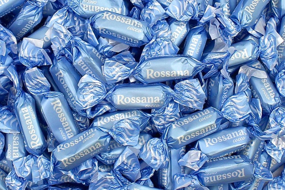 Primo piano di numerose Caramelle Rossana Cocco sfuse nel loro incarto colore azzurro con scritta e logo a contrasto colore bianco