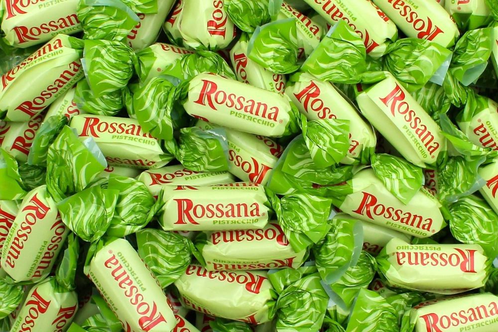 Primo piano di numerose Caramelle Rossana Pistacchio sfuse nel loro incarto verde con scritta e logo in rosso.