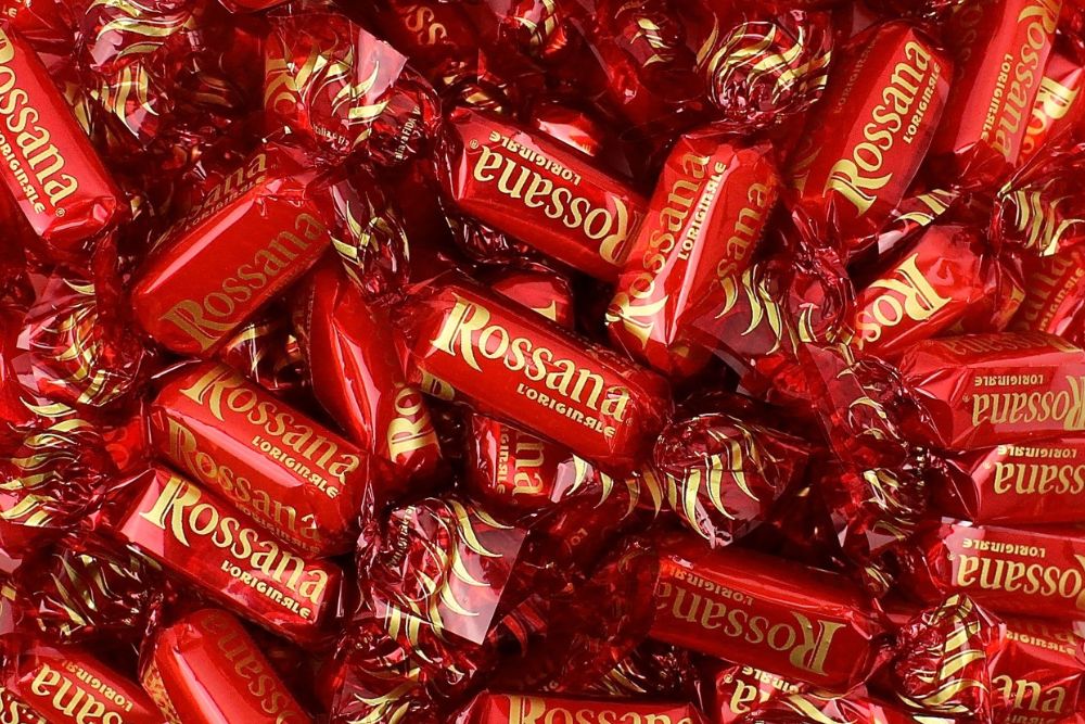 Primo piano di numerose caramelle sfuse Rossana l’Originale incartate nell’iconico incarto rosso con scritta e logo dorati.