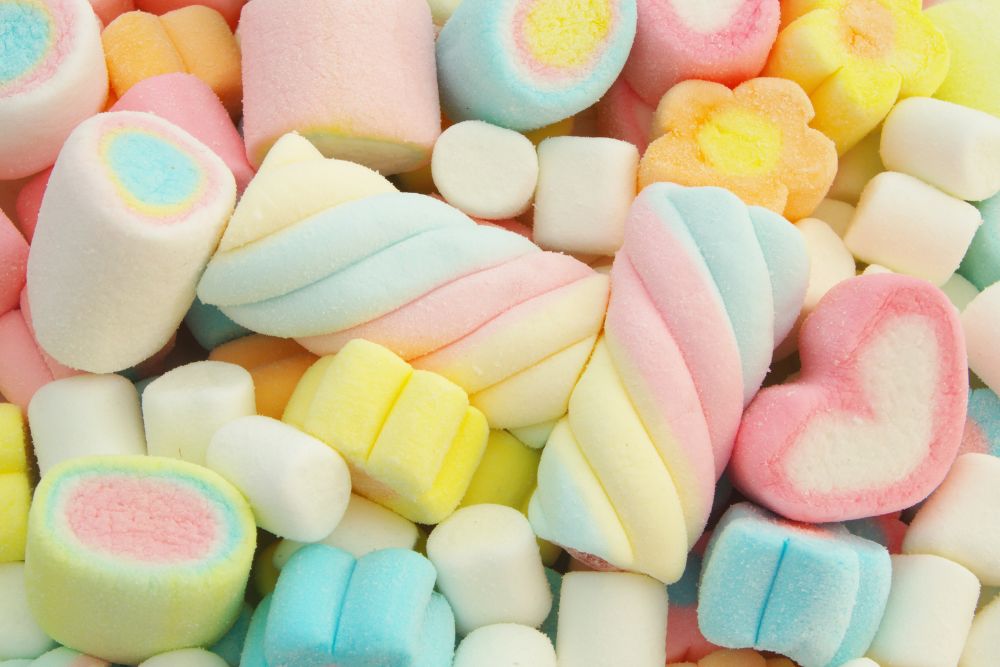 Un assortimento di marshmallow colorati con forme a spirale, treccia, cuore e fiore in tonalità pastello.