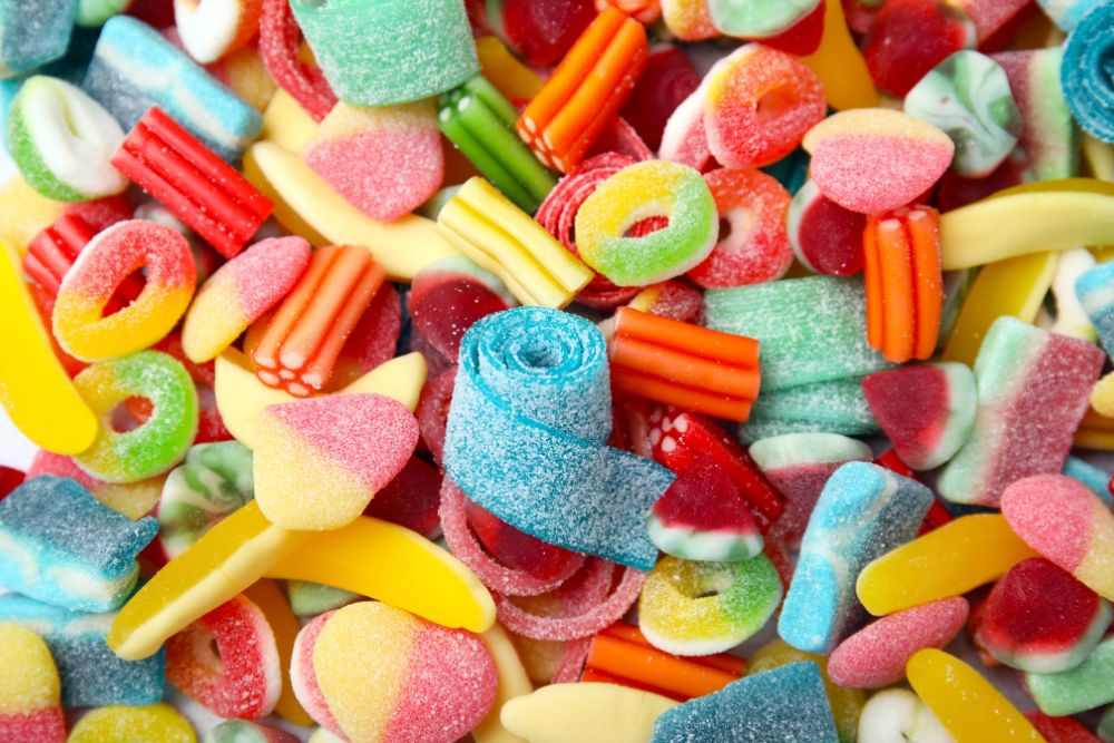 Variegata selezione di caramelle gommose colorate con zucchero, tra cui anelli, bastoncini e forme fruttate.