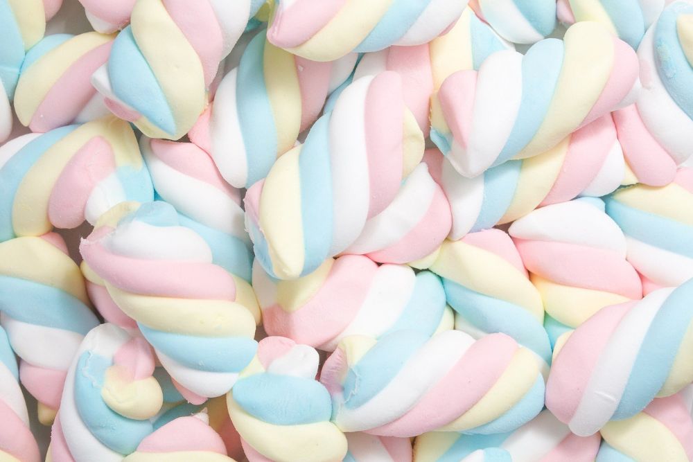 Marshmallow a treccia soffici e colorati con strisce rosa, azzurre e gialle, disposti in un mucchio compatto.