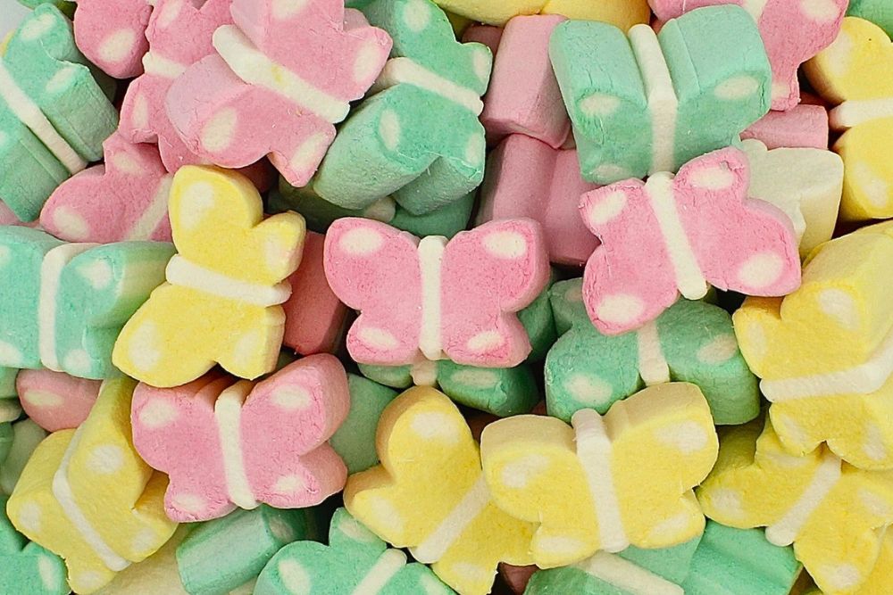 Soffici marshmallow a forma di farfalla in colori pastello rosa, giallo e verde, disposte in modo casuale.