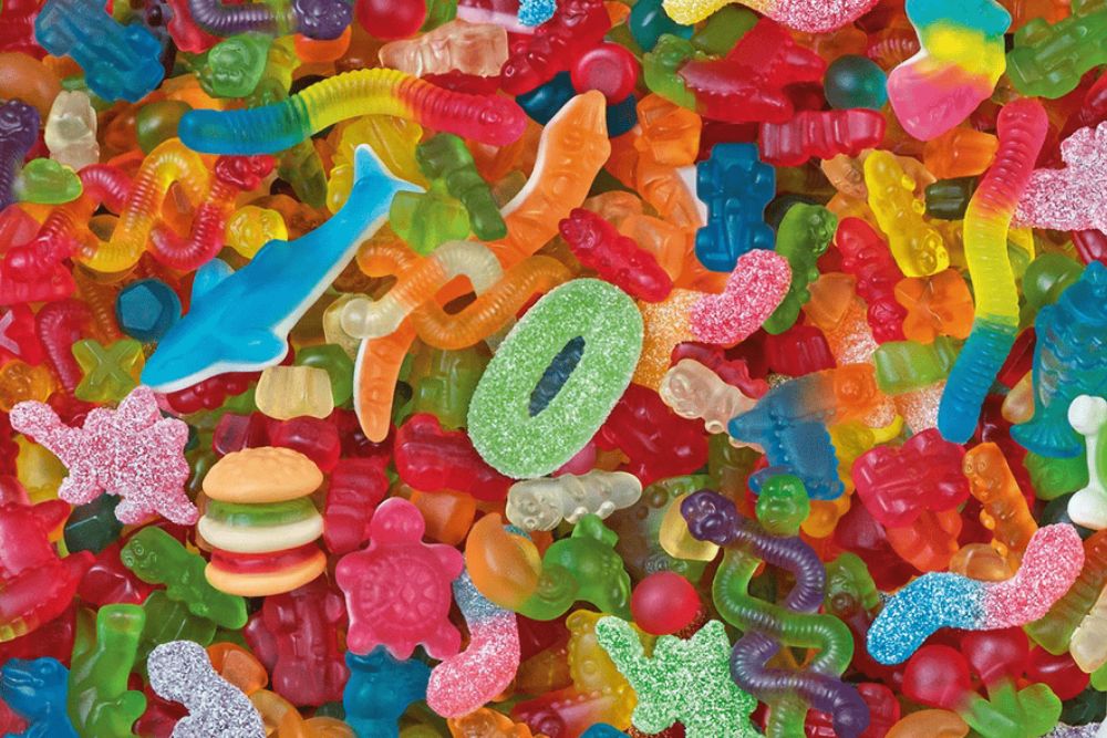 Varietà colorata di caramelle gommose di diverse consistenze lucide e zuccherate a forma di vermi, orsetti, hamburger e animali in un mix vivace.