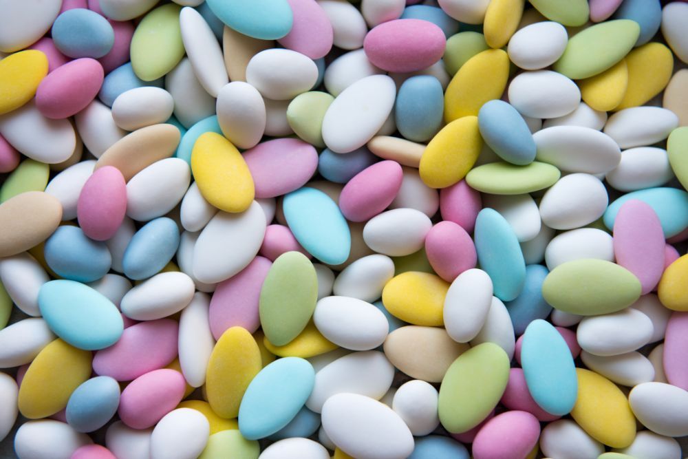 Confetti di mandorla colorati in tonalità pastello come rosa, azzurro, giallo, verde e confetti bianchi disposti alla rinfusa in modo casuale.