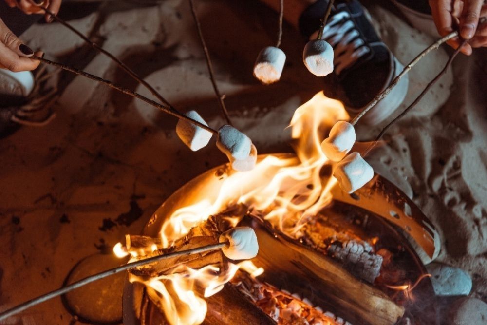 Marshmallow bianchi infilzati su bastoncini arrostiti su un falò acceso sulla sabbia di notte.