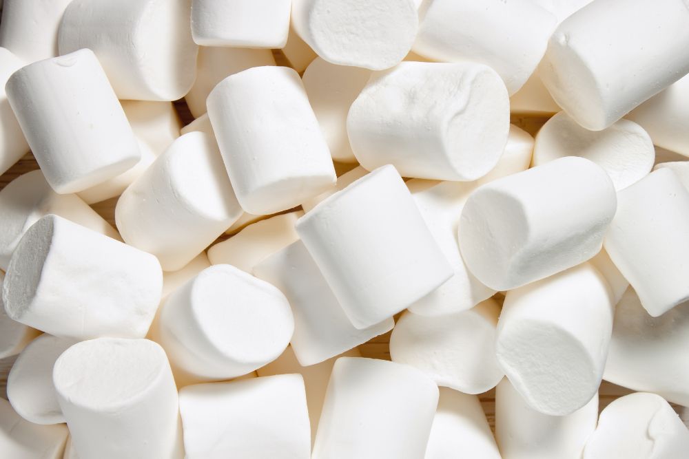 Marshmallow bianchi soffici e cilindrici disposti in modo casuale su una superficie.