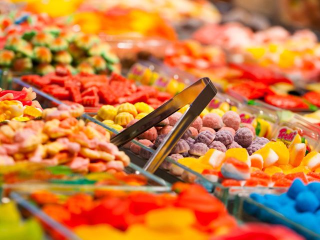 Un colorato allestimento di dolciumi sfusi, con pinze di metallo appoggiate tra eleganti contenitori trasparenti in vetro pieni di caramelle gommose di varie tipologie, forme e colori per creare una scena vivace e invitante.