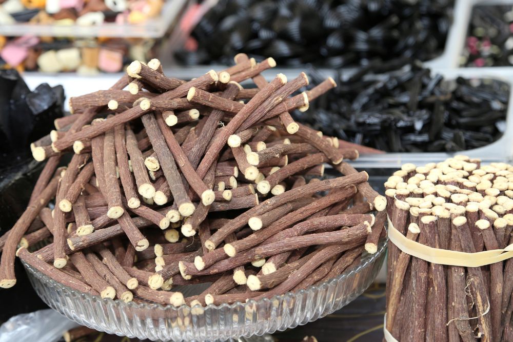 Ciotola di vetro piena di bastoncini di liquirizia naturale tagliati, con mazzi legati accanto e caramelle alla liquirizia assortite sullo sfondo.