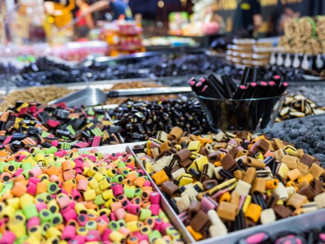 Vassoi assortiti di caramelle alla liquirizie colorate e di varie forme in un mercato affollato.
