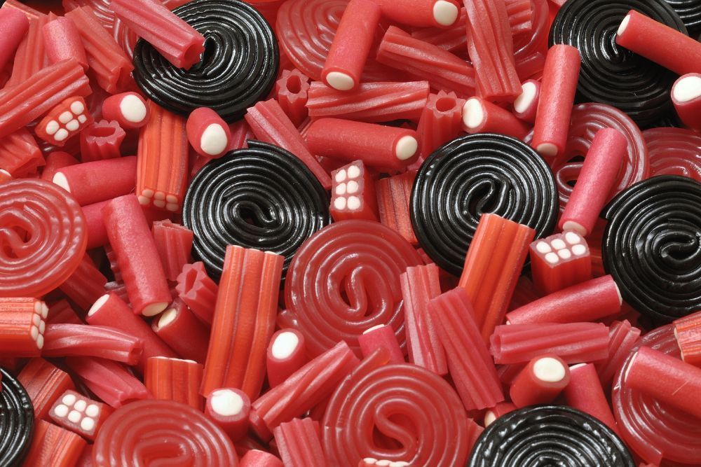 Caramelle di liquirizia rossa e nera assortite, con forme a spirale e bastoncini ripieni bianchi.