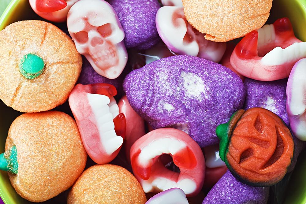 Caramelle gommose di Halloween a forma di zucche arancioni, denti di vampiro, teschi bianchi e viola di marshmallow in una ciotola.