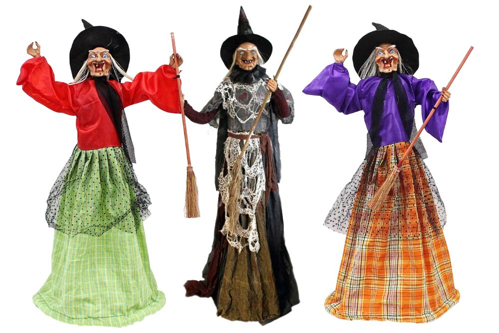 Tre colorate bambole-strega a dimensione naturale, con costumi rossi, neri e viola, facce spiritate, cappelli a punta a tesa larga e mani alzate che brandiscono le loro scope.
